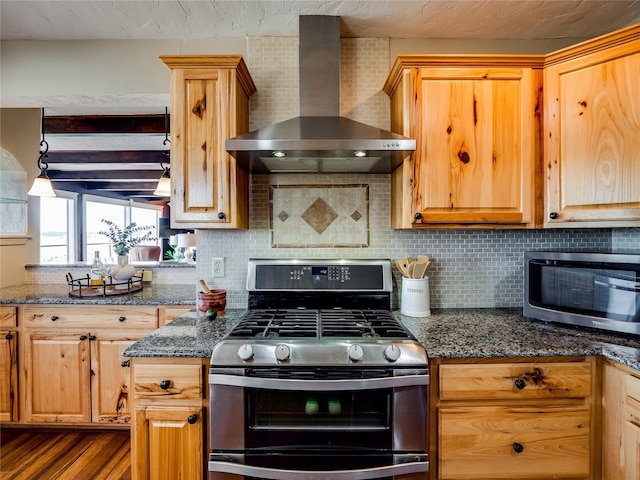 kitchen with decorative backsplash, appliances with stainless steel finishes, dark stone counters, and wall chimney range hood