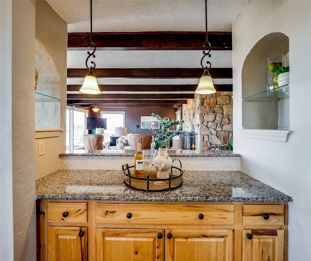 kitchen with beam ceiling, dark stone countertops, pendant lighting, and a textured ceiling