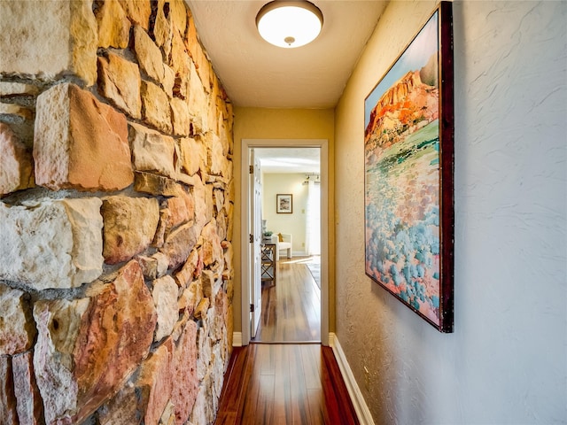 hall featuring baseboards, wood finished floors, and a textured wall