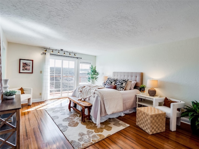 bedroom with a textured ceiling, hardwood / wood-style floors, rail lighting, and access to outside