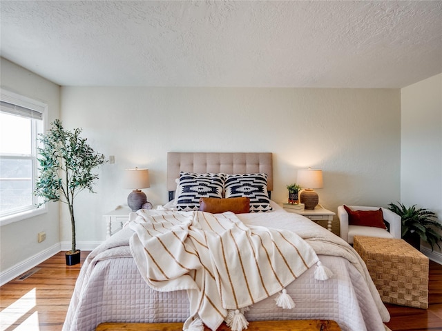 bedroom with visible vents, wood finished floors, baseboards, and a textured ceiling