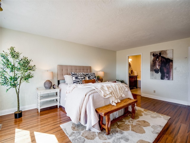 bedroom with connected bathroom, a textured ceiling, baseboards, and wood finished floors