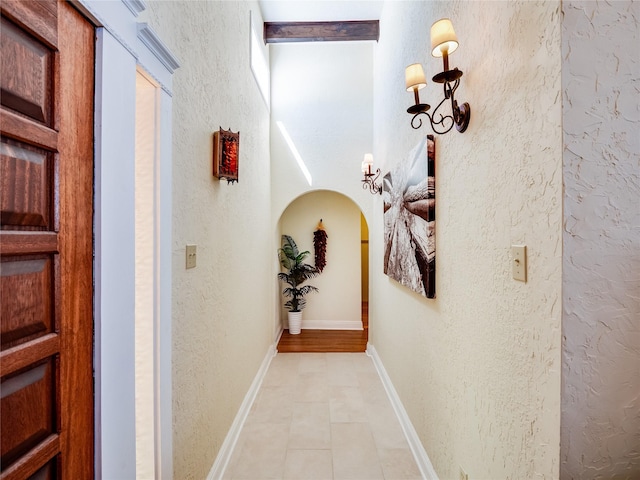 hallway featuring light tile patterned floors, a textured wall, baseboards, and arched walkways