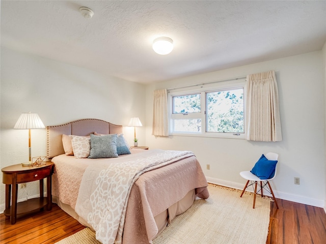 bedroom featuring baseboards, a textured ceiling, and wood finished floors