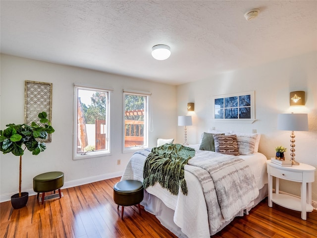 bedroom featuring visible vents, baseboards, a textured ceiling, and hardwood / wood-style flooring