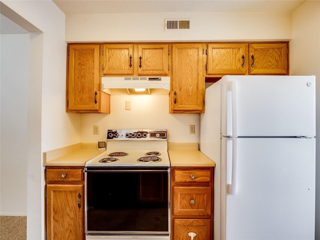 kitchen featuring visible vents, under cabinet range hood, light countertops, range with electric stovetop, and freestanding refrigerator