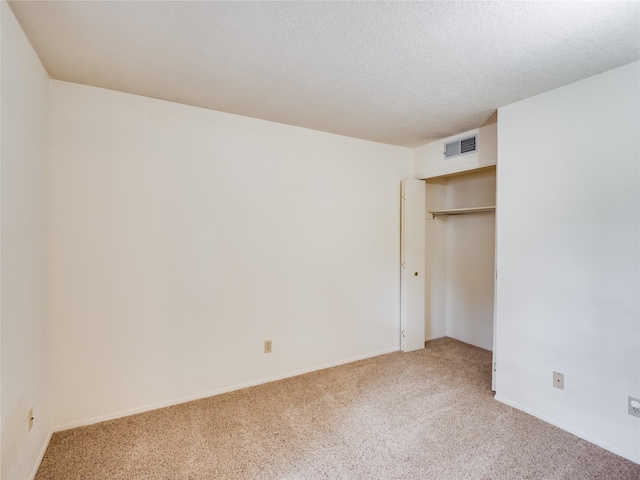 unfurnished bedroom featuring a textured ceiling, visible vents, a closet, and light carpet