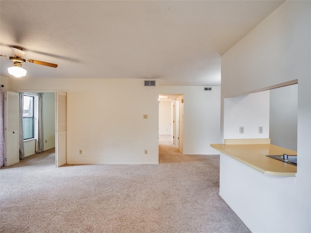 unfurnished living room featuring a ceiling fan, light colored carpet, and visible vents