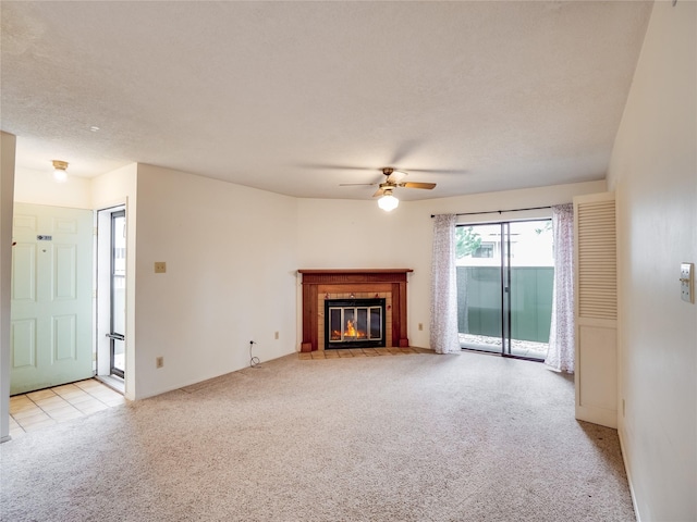 unfurnished living room with ceiling fan, a textured ceiling, a tile fireplace, and light carpet