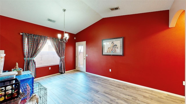 dining room with a notable chandelier, visible vents, wood finished floors, and vaulted ceiling