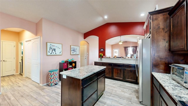 kitchen with lofted ceiling, arched walkways, freestanding refrigerator, dark brown cabinetry, and light wood-style floors