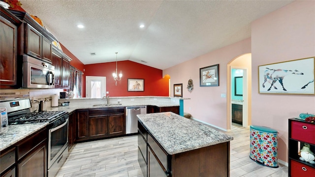 kitchen with a peninsula, lofted ceiling, a sink, stainless steel appliances, and dark brown cabinetry