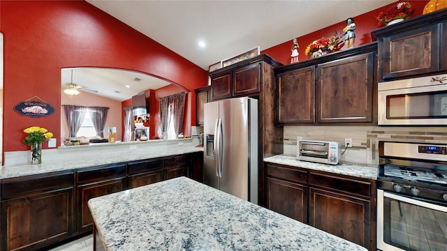 kitchen featuring backsplash, light stone countertops, a toaster, lofted ceiling, and appliances with stainless steel finishes