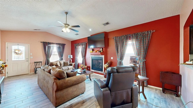 living room featuring vaulted ceiling, visible vents, light wood-style flooring, and a glass covered fireplace