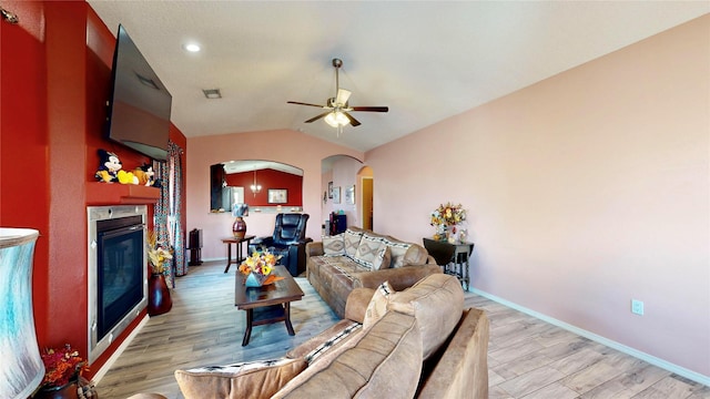 living room featuring lofted ceiling, light wood-style flooring, a fireplace, and arched walkways