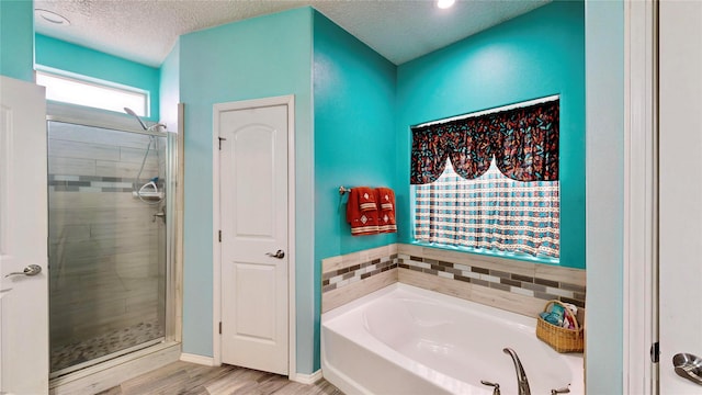 full bathroom featuring a shower stall, a textured ceiling, a garden tub, and wood finished floors