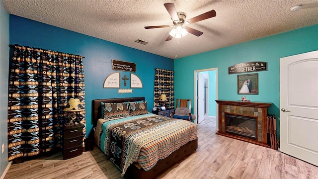 bedroom with visible vents, a fireplace, a textured ceiling, and wood finished floors