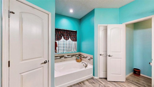 full bath with baseboards, a textured ceiling, wood finished floors, and a bath