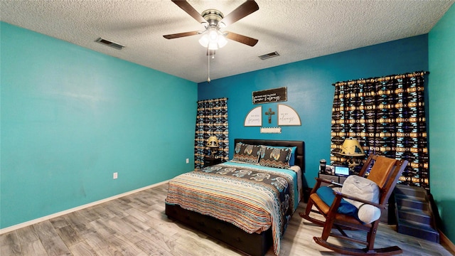 bedroom featuring visible vents, a textured ceiling, baseboards, and wood finished floors