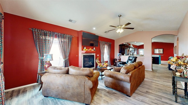 living room with visible vents, vaulted ceiling, wood finished floors, arched walkways, and a glass covered fireplace