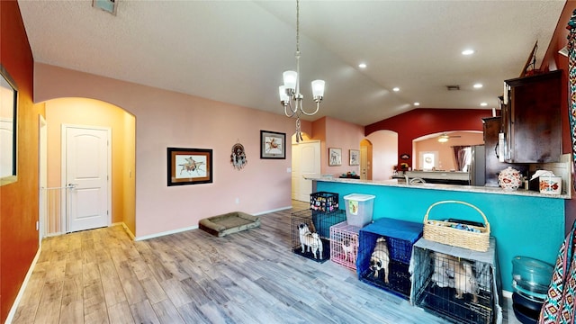 kitchen featuring arched walkways, light wood finished floors, freestanding refrigerator, and vaulted ceiling