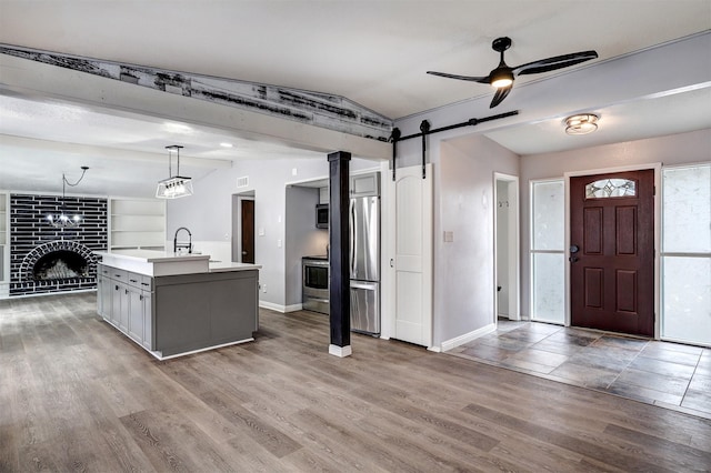 kitchen with a ceiling fan, wood finished floors, stainless steel appliances, light countertops, and a barn door