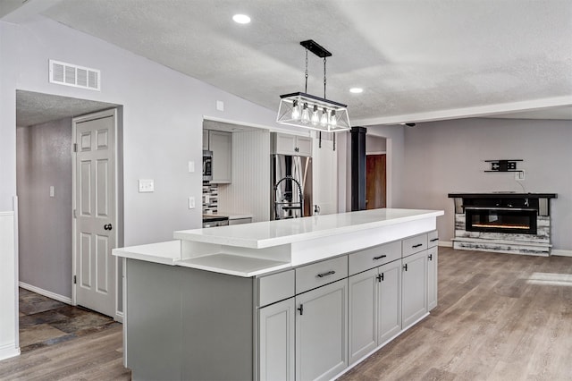 kitchen with light wood-type flooring, visible vents, gray cabinetry, a glass covered fireplace, and appliances with stainless steel finishes