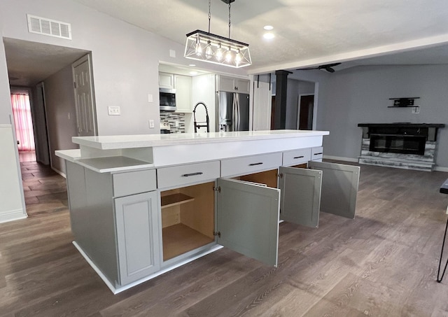 kitchen with visible vents, dark wood-type flooring, a kitchen island with sink, a glass covered fireplace, and stainless steel appliances