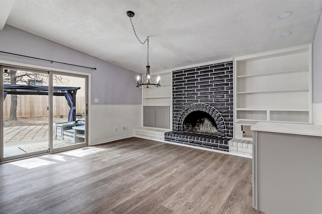 unfurnished living room with vaulted ceiling, a fireplace, a textured ceiling, and wood finished floors