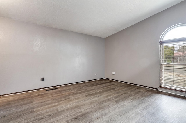 empty room with visible vents, lofted ceiling, a textured ceiling, and wood finished floors