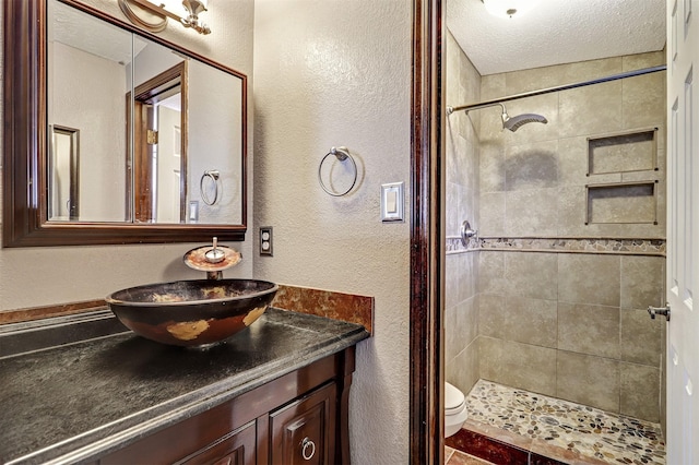 full bath with toilet, a textured ceiling, a shower stall, vanity, and a textured wall