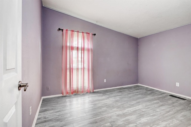 spare room featuring wood finished floors, visible vents, and baseboards