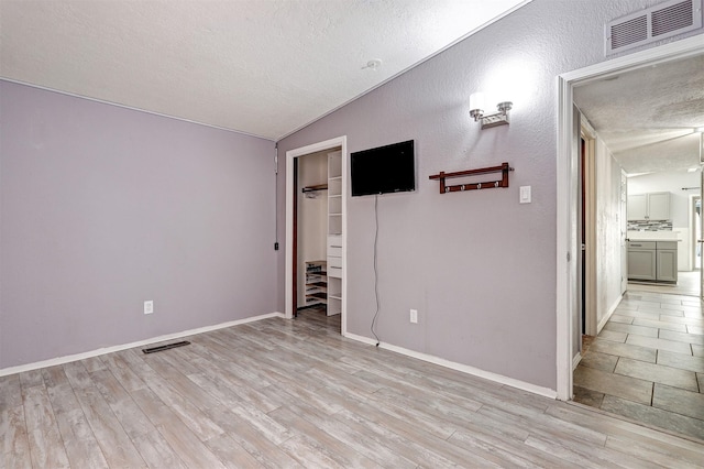 interior space with baseboards, visible vents, light wood-style flooring, a spacious closet, and a textured ceiling