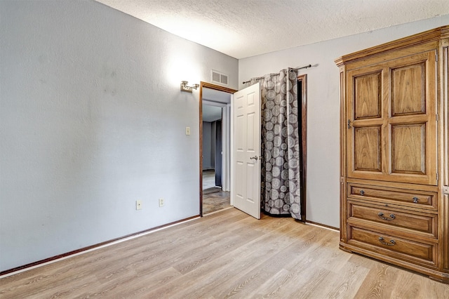 unfurnished bedroom with visible vents, baseboards, light wood-style floors, and a textured ceiling