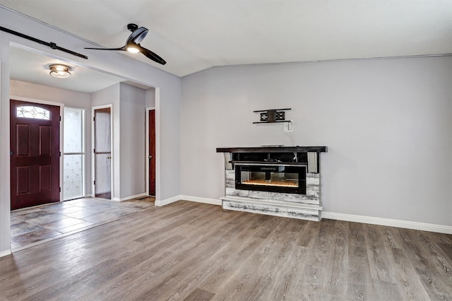 unfurnished living room featuring lofted ceiling, wood finished floors, a glass covered fireplace, baseboards, and ceiling fan