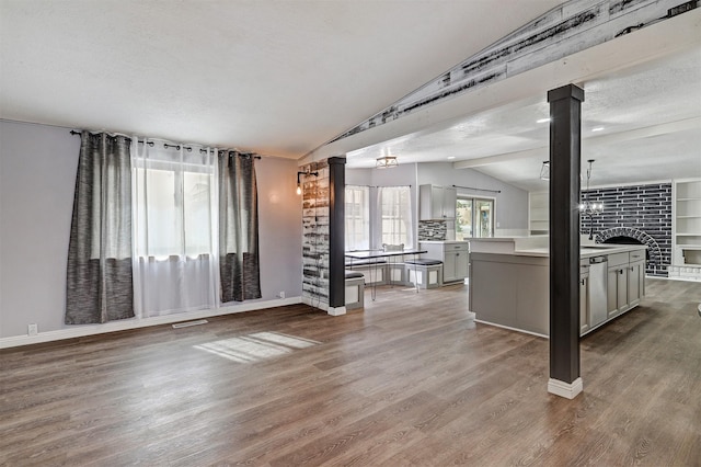 unfurnished living room with visible vents, lofted ceiling, wood finished floors, a textured ceiling, and ornate columns