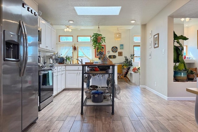 kitchen with a skylight, light wood-style flooring, appliances with stainless steel finishes, and white cabinetry