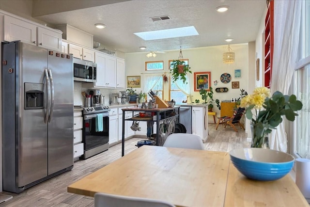 kitchen with visible vents, light wood-type flooring, appliances with stainless steel finishes, a skylight, and white cabinets