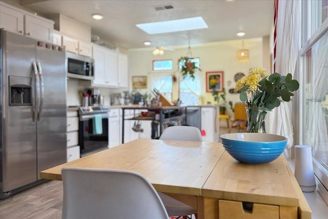 kitchen with light wood-style floors, appliances with stainless steel finishes, a skylight, and white cabinets