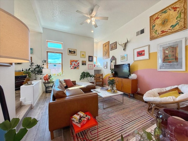 living area featuring a ceiling fan, wood finished floors, visible vents, and a textured ceiling