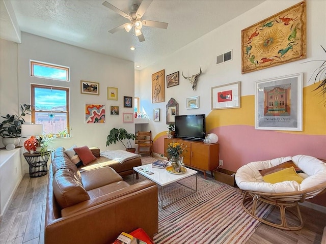 living room with visible vents, a ceiling fan, a textured ceiling, wood finished floors, and baseboards