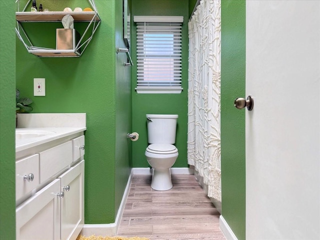 bathroom with toilet, vanity, baseboards, and wood finished floors