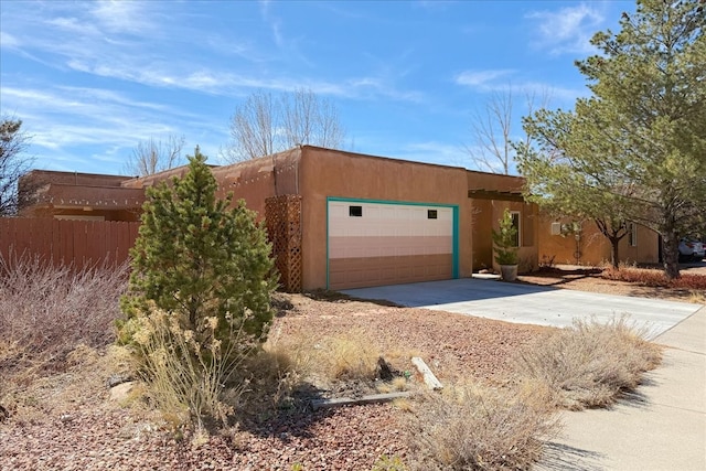 view of front of home with stucco siding, an attached garage, concrete driveway, and fence