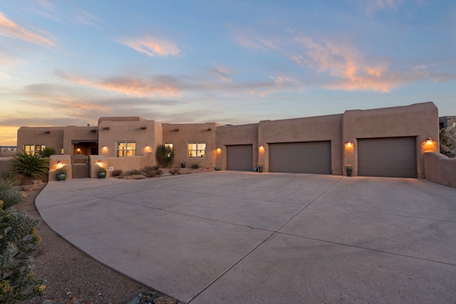 pueblo-style house with concrete driveway, a gate, an attached garage, and stucco siding