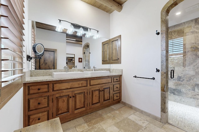 bathroom with beam ceiling, a stall shower, stone tile floors, baseboards, and vanity