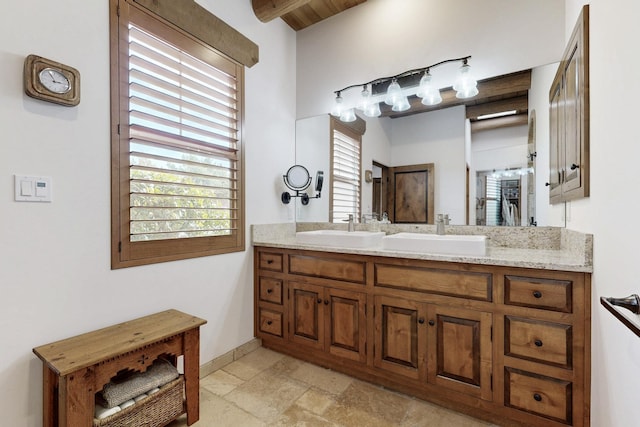 full bath featuring stone tile flooring, double vanity, baseboards, and a sink