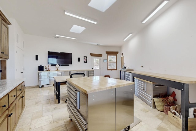 kitchen featuring stone tile flooring, butcher block counters, a center island, and baseboards