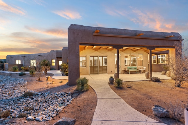 back of property at dusk featuring a patio area and stucco siding