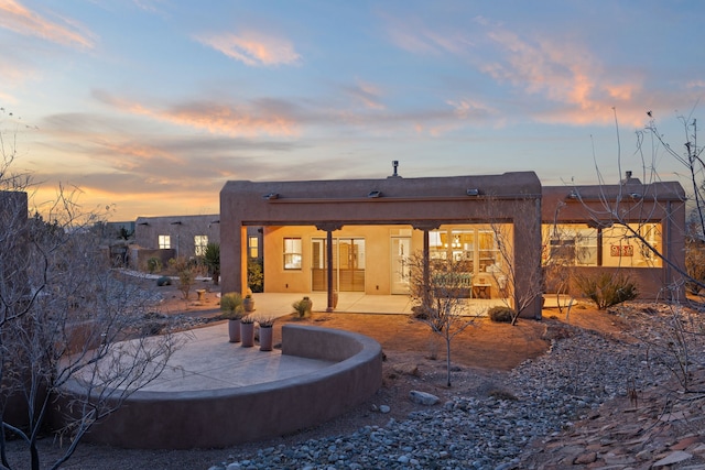 back of house at dusk with a patio area and stucco siding