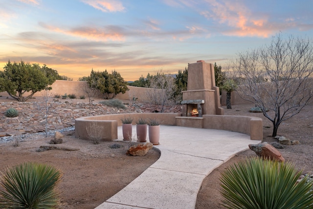 view of patio / terrace featuring concrete driveway, fence, and a warm lit fireplace